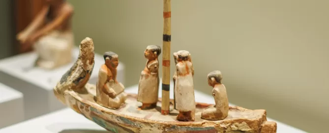 MAEC Cortona collezione egizia. Modello di barca funeraria. Lo scafo è dipinto a bande verde-blu e rosso, l'albero è a fondo bianco con fasce alternativamente rosse e nere. Ci sono 5 statuine maschili fissate con tenoni, una delle quali raffigura il defunto.