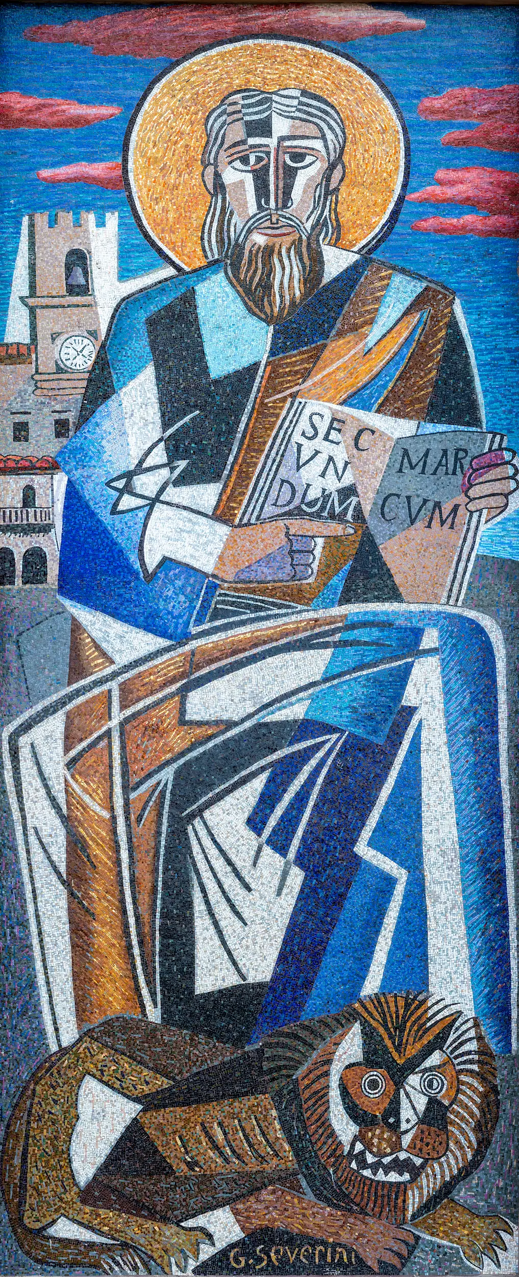 Mosaico di San Marco realizzato da Gino Severini per la facciata della Chiesa di San Marco a Cortona. Al centro è raffigurato l'evangelista seduto in trono, con una grande aureola dorata attorno al capo. Indossa una veste composta da ampie forme geometriche nei toni del blu, dell'azzurro, del bianco e dell'oro e tiene aperto il Vangelo con l'iscrizione latina “Secundum Marcum”. Ai suoi piedi è rappresentato il leone alato, simbolo di San Marco. Sullo sfondo compaiono il Palazzo Comunale di Cortona e un cielo azzurro attraversato da nuvole rosate. Le figure sono costruite attraverso forme geometriche e colori brillanti che uniscono il linguaggio del Cubismo alla tradizione del mosaico bizantino.